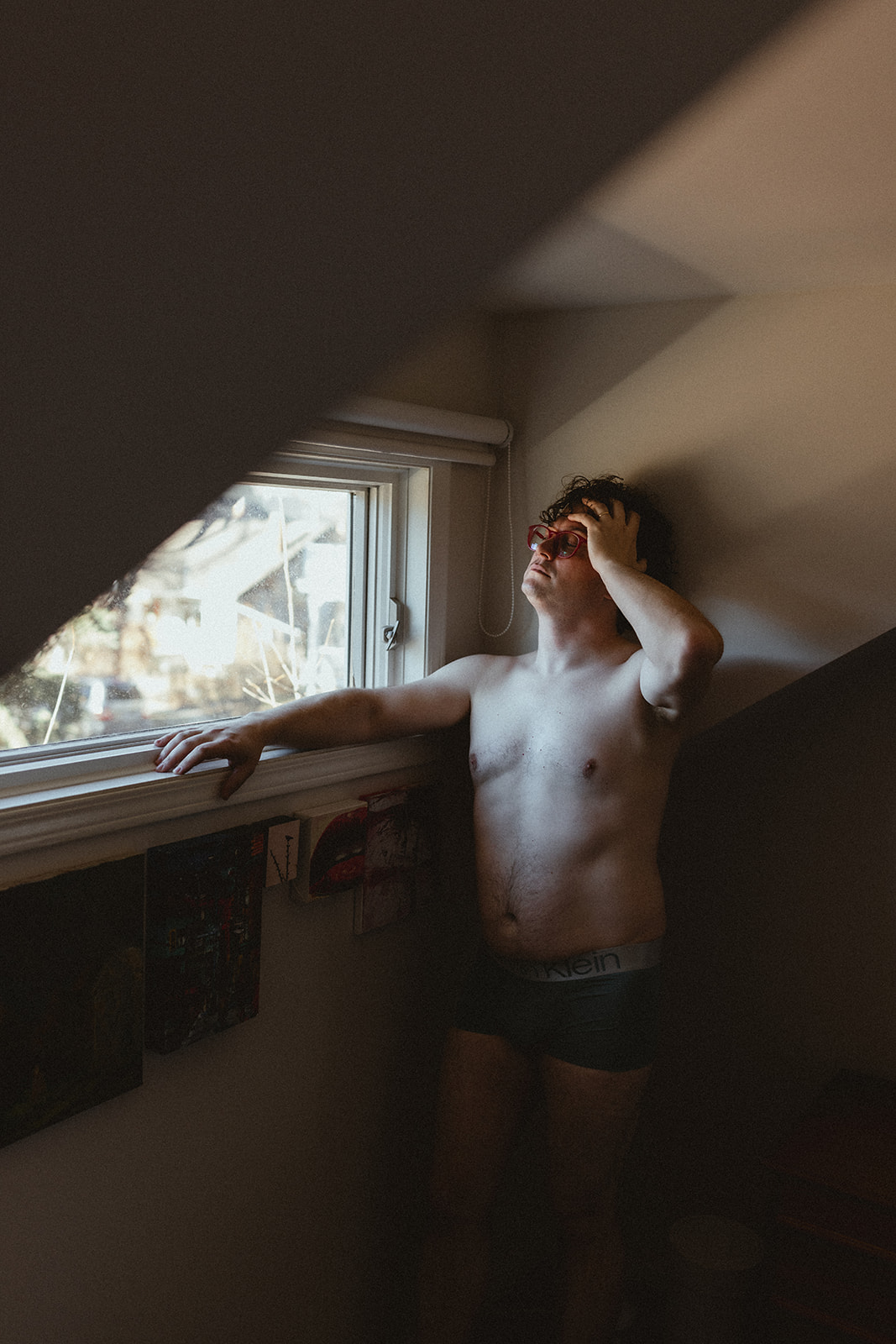 young man standing under a window in his boxers