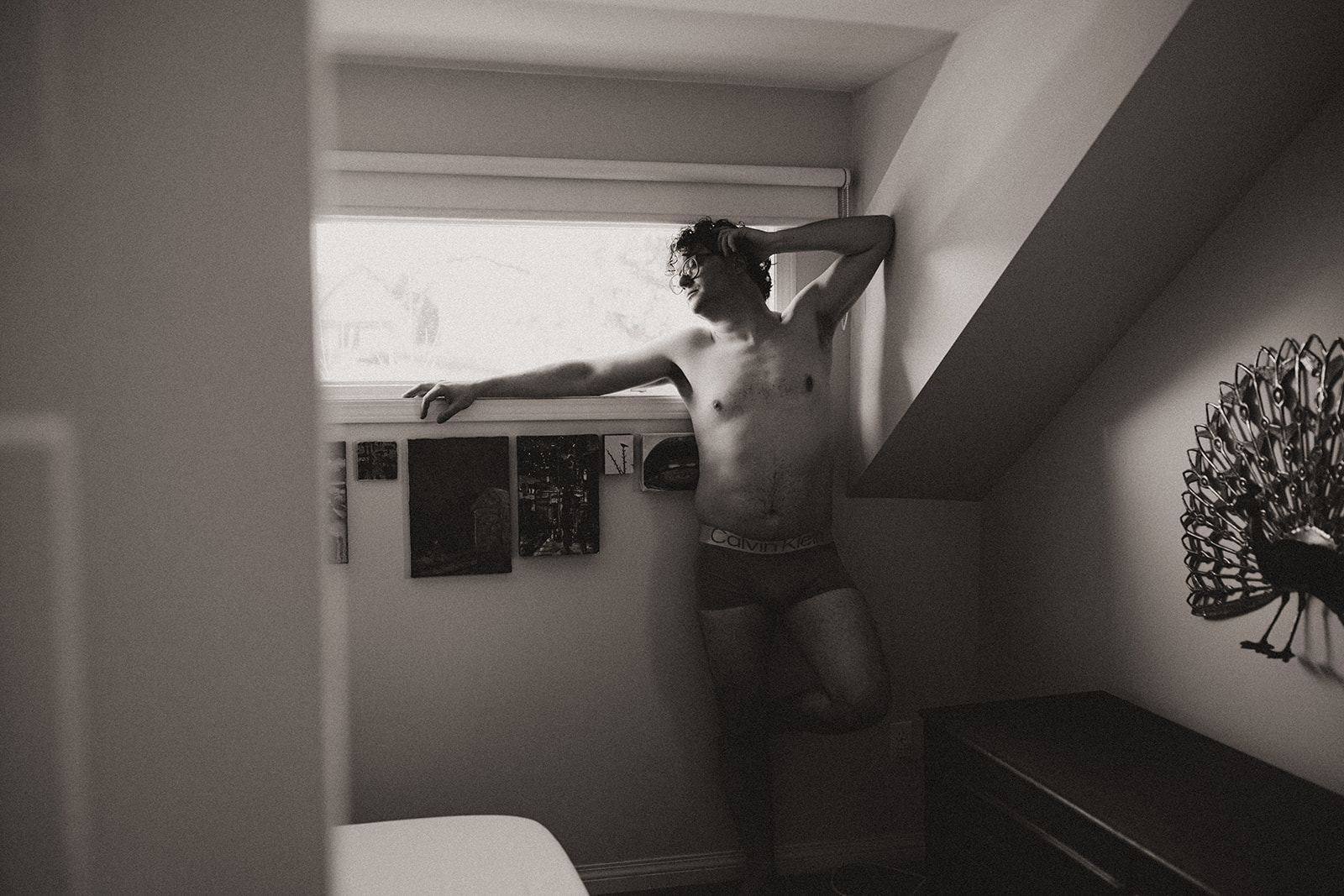 young man standing under a window in his boxers