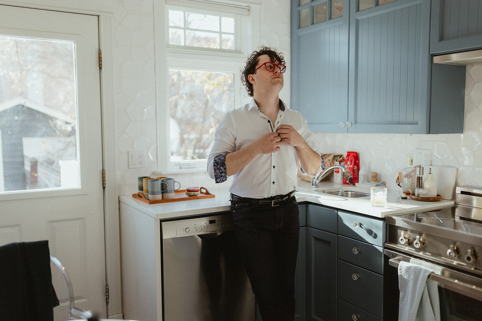 young man standing in his Alberta home kitchen unbuttoning his shirt